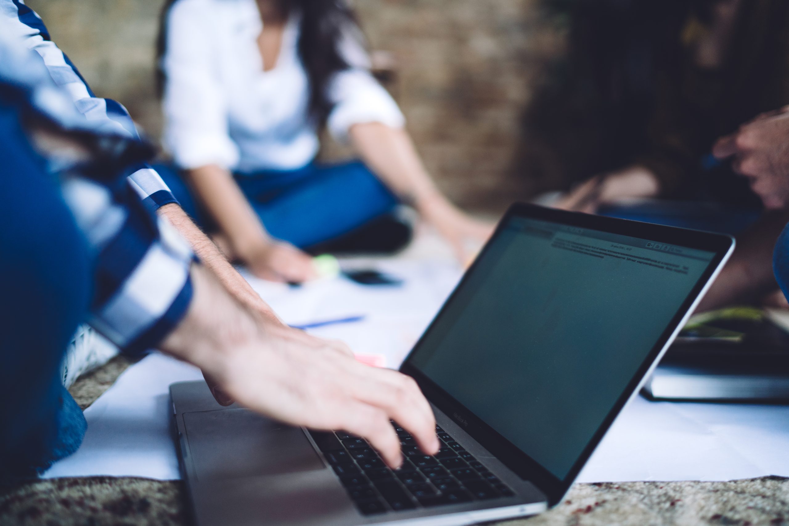 Side view of anonymous guy in casual wear sitting on floor and typing on keyboard of laptop while working remotely in modern apartment
